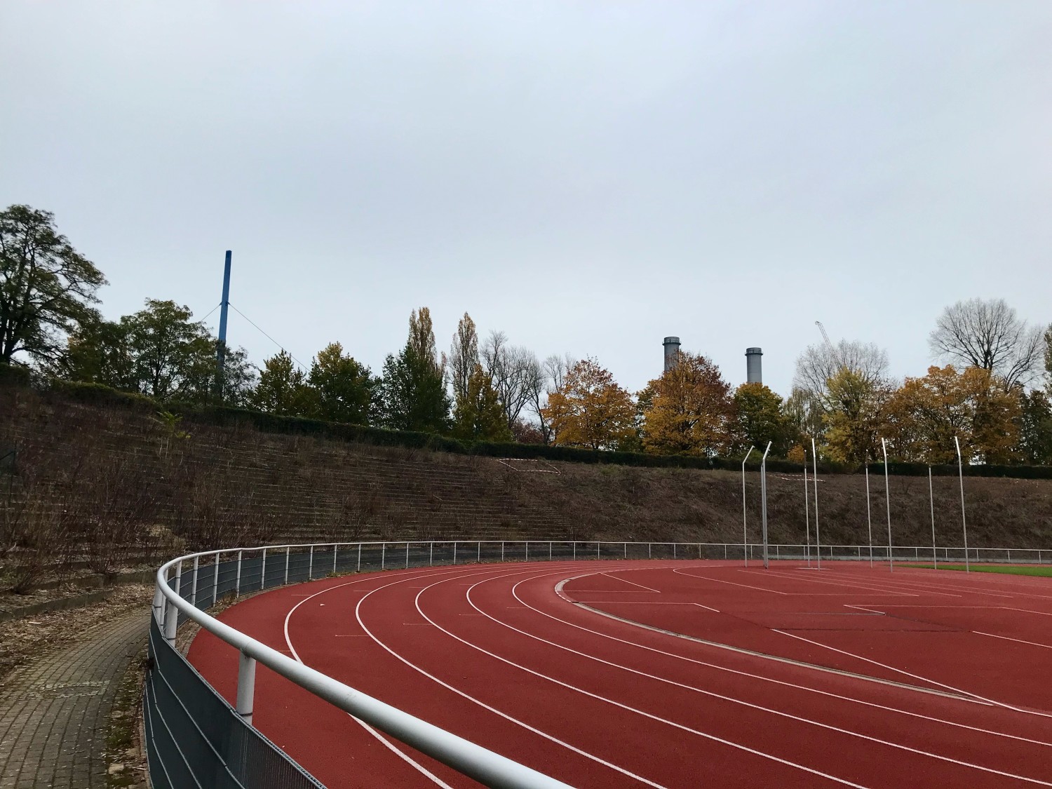 Tartanbahn der Ostkurve im Stadion Wilmersdorf mit markierten Aussaatflächen auf der Böschung im Hintergrund.