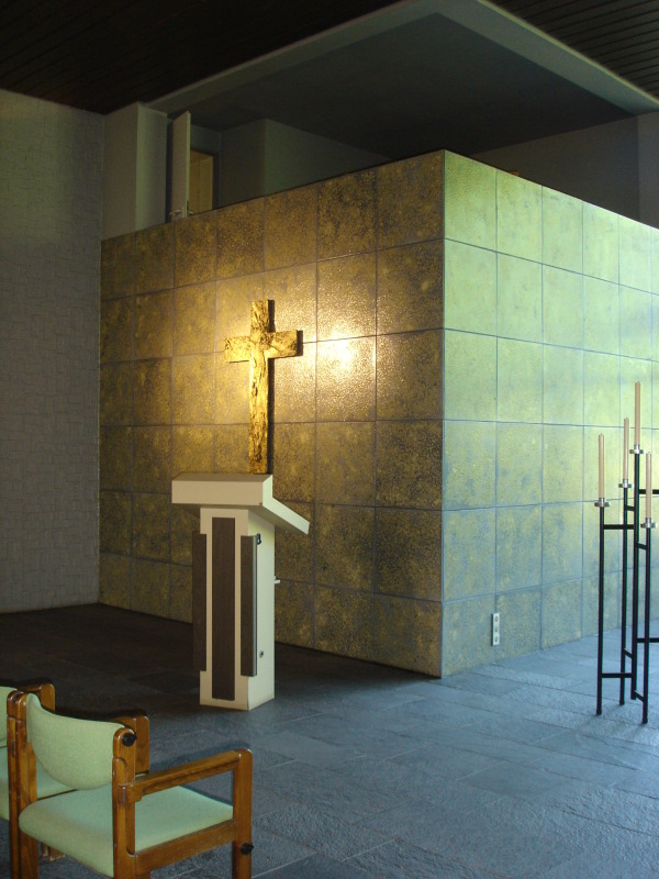 Ansicht des Rednerbereichs in der Feierhalle Gatow, dunkler Steinboden, goldene Wand mit Kreuz, weißes Pult