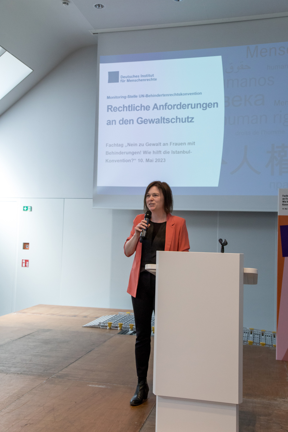 Dr. Britta Schlegel vom Deutschen Institut steht auf der Bühne und hält einen Vortrag. Auf der Leinwand hinter der Bühne steht der Titel des Vortrags "Rechtliche Anforderungen an den Gewaltschutz"