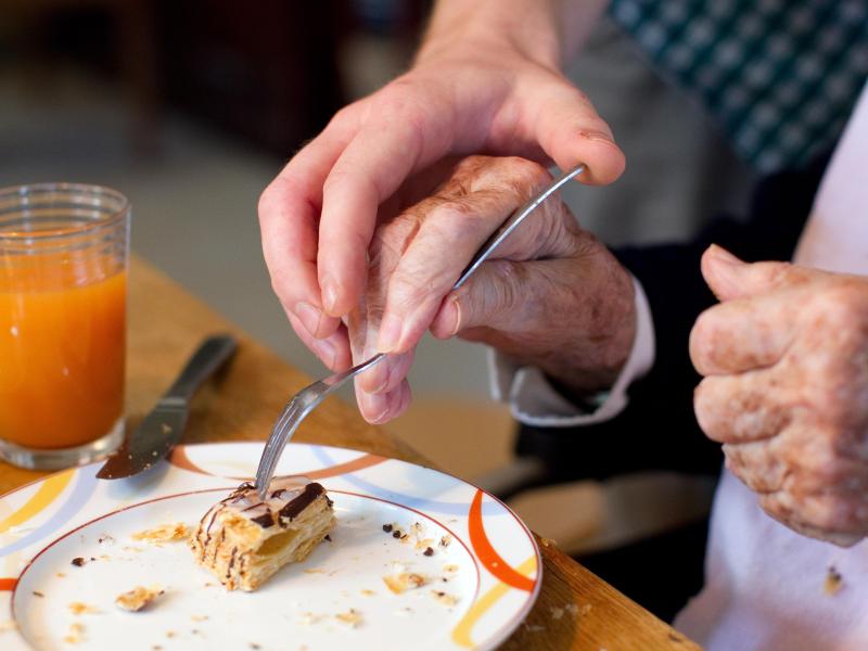Mann hilft einer älteren Frau beim Einnehmen einer Mahlzeit