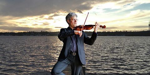 Ein Mann spielt Geige, hinter ihm ist das Meer zu sehen