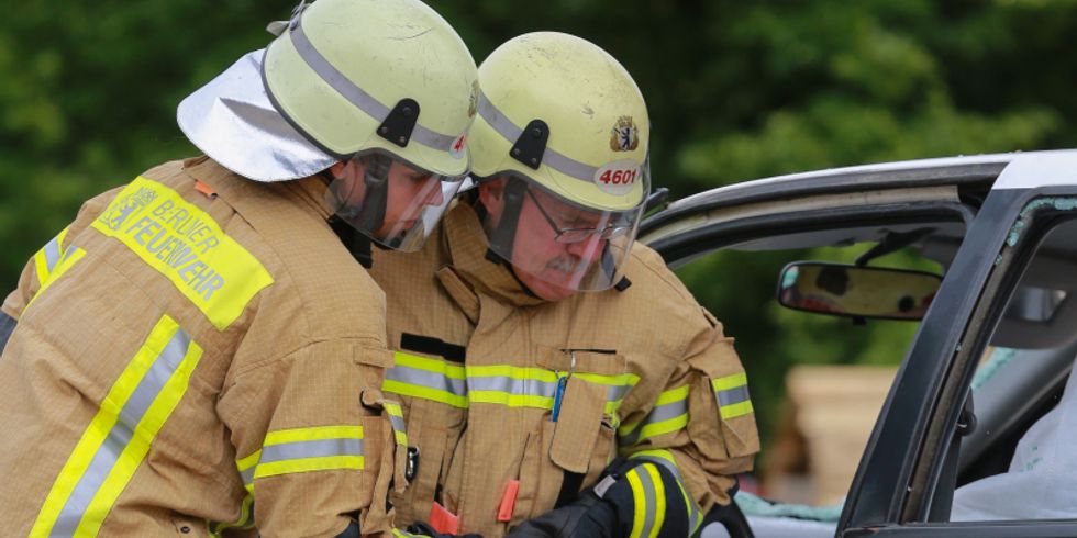 Zwei Feuerwehrmänner schneiden ein Auto auf