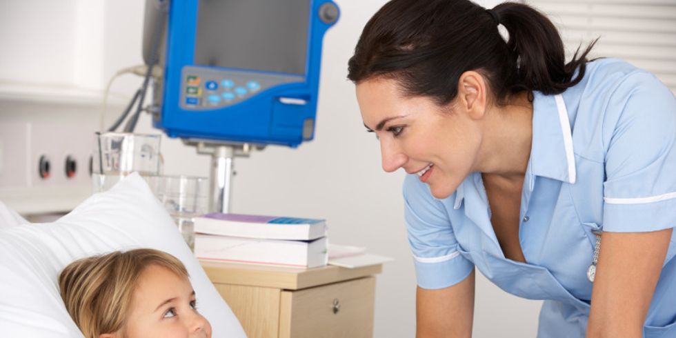 Krankenschwester steht am Krankenbett eines lächelnden Mädchens