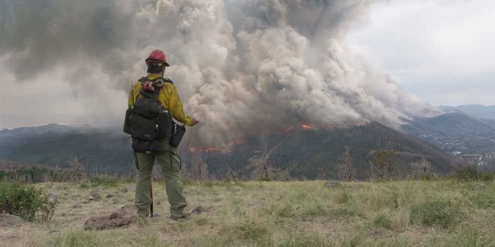 Aus dem Film „No Way Out - gegen die Flammen“ - Feuerwehrmann steht im Gebirge - im Hintergrund brennt Wald 