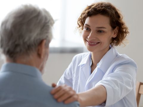 Lächelnde Ärztin beruhigt und untersucht einen Senioren im Krankenhaus
