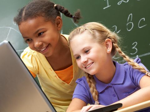 zwei Kinder vor einem Laptop mit Tafel im Hintergrund