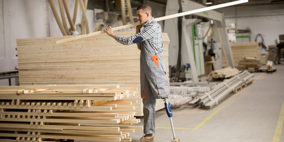 Behinderter junger Mann mit künstlichem Bein arbeitet in der Möbelfabrik