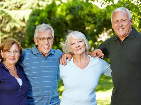 Zwei Seniorinnen und zwei Senioren stehen nah beieinander in einem Park und lächeln in die Kamera
