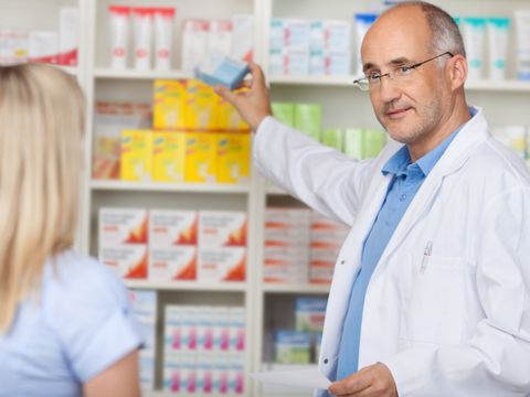 Apotheker greift nach einer Medikamentenpackung für eine Kundin