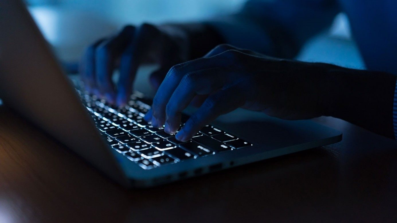 Hände auf einer beleuchteten Laptoptastatur im abgedunkelten Raum