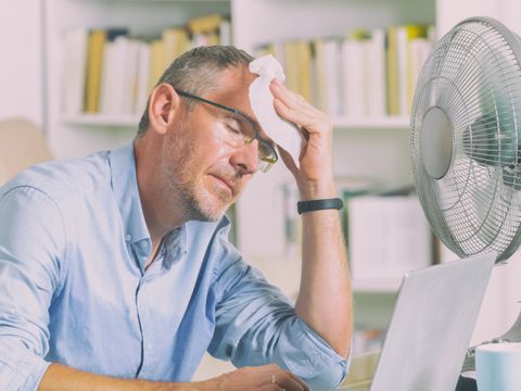 älterer Mann vor Ventilator tupft sich Schweiß von der Stirn