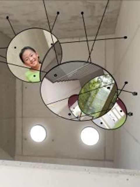 Runde Spiegel in einem Treppenhaus von der Decke hängend, so dass Eindrücke von der tieferliegenden Treppenpartie und Draußen widergespiegelt werden.