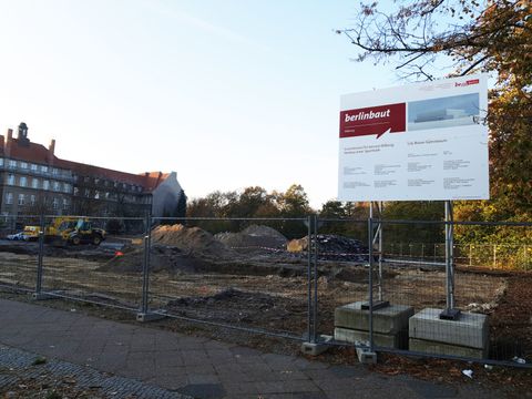 Bildvergrößerung: Blick auf die für den Bau geebnete Baufläche mit dem Bauschild im Vordergrund und dem Lily-Braun-Gymnasium im Hintergrund