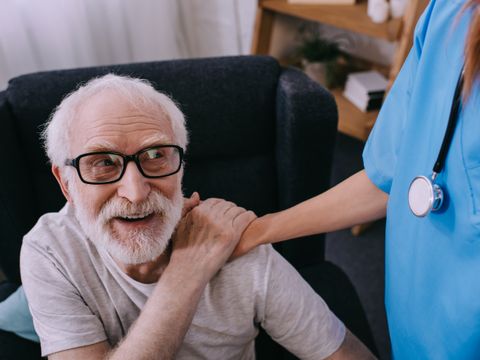Pflegekraft legt die Hand auf die Schulter eines älteren Mannes