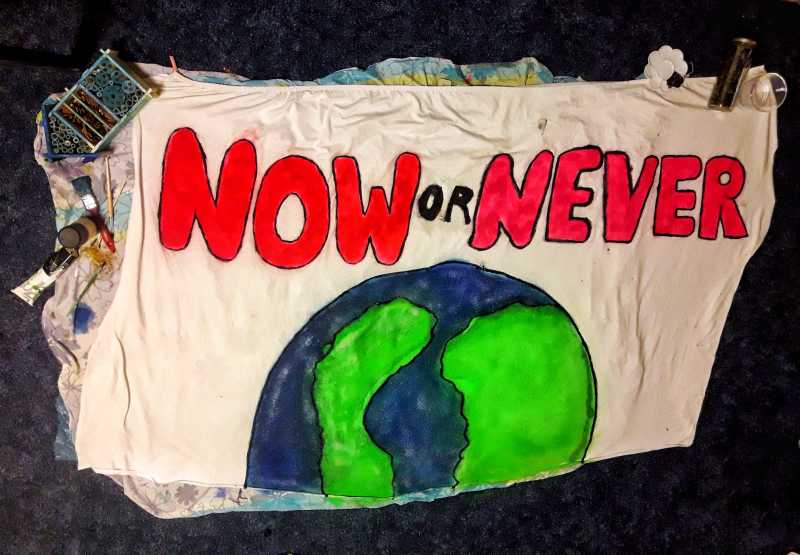 Ein Textilbanner mit einer Darstellung des Planeten Erde, darüber prangt der Schriftzug "Now or Never"