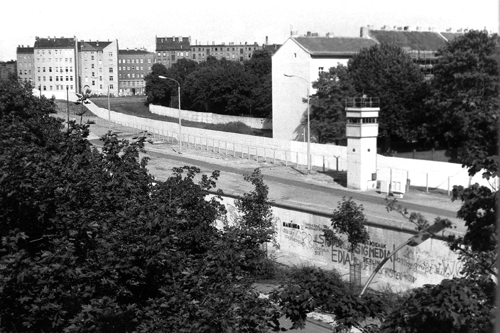 Bernauer Straße in Höhe der Ackerstraße in den späten 1980er Jahren: Die Versöhnungskirche wurde 1985 entfernt und die Grenzanlagen zeigen einen fertigen Stand mit vorderer Mauer entlang der Bernauer Straße, diversen Sperranlagen, Postenweg, Kontrolltürmen, Grenzsignalzaun und Hinterlandmauer.