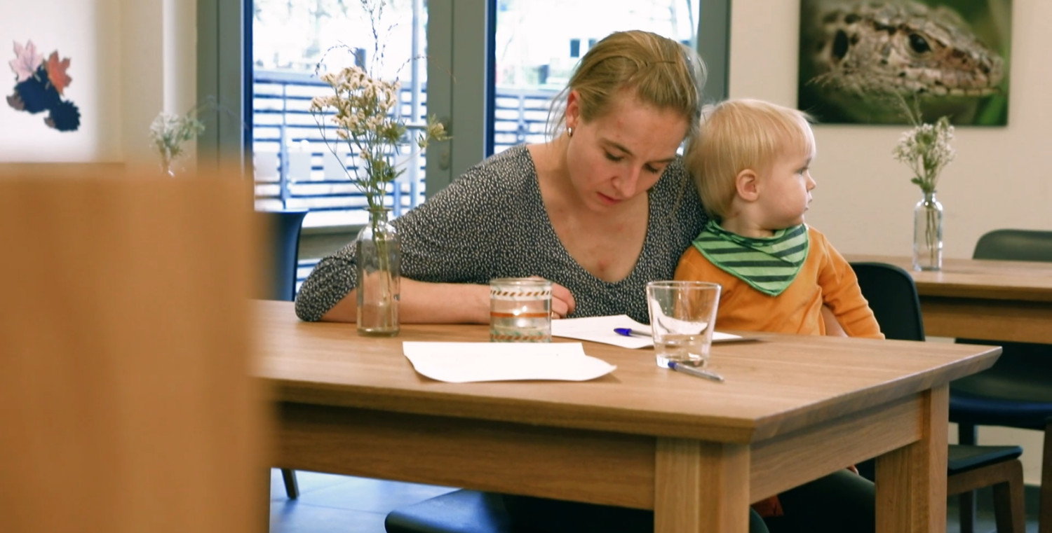 Eine Frau mit einem Kind auf dem Schoß liest etwas am Tisch