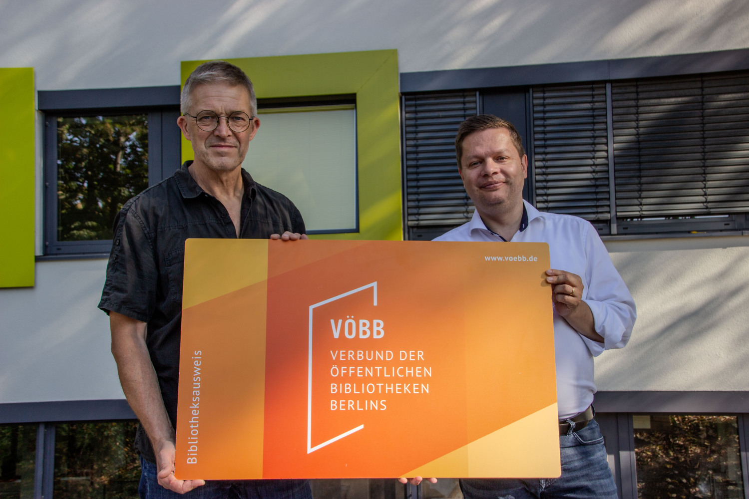 Bezirksbürgermeister Martin Schaefer (rechts) gemeinsam mit dem Schulleiter der Hermann-Gmeiners-Schule Ullrich Negraszus (links) und dem symbolischen Bibliotheksausweis