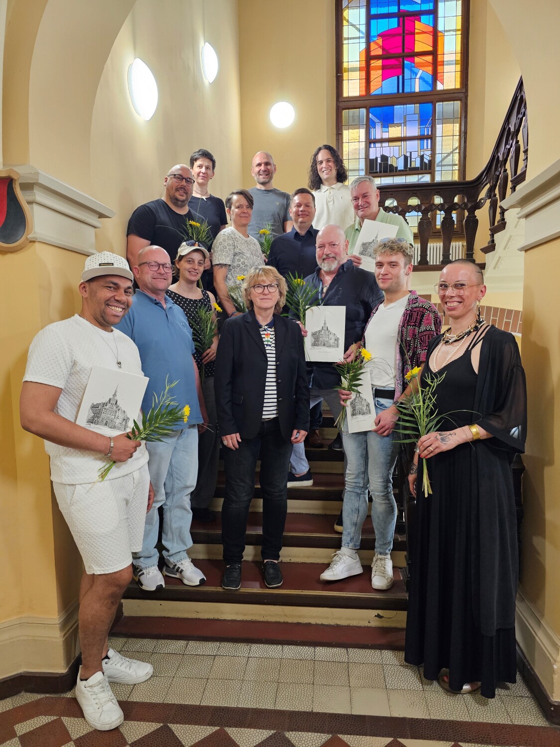 Berufung des Queer-Beirates durch den Bezirksbürgermeister Martin Schaefer. Die Mitglieder des Queer-Beirates stehen gemeinsam mit dem Bezirksbürgermeister, Martin Schaefer, und der Diversity- und Queer-Beauftragten, Sabine Pöhl, auf einer Treppe vor dem Ratssaal.