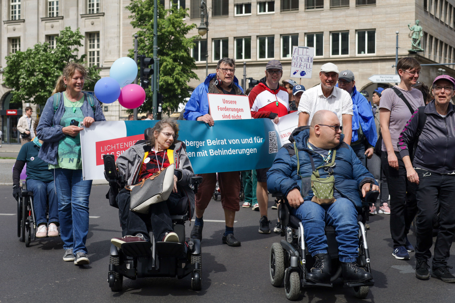 Mitglieder des Wohn-Beirates Wilde Füchse tragen das Banner vom Lichtenberger Beirat von und für Menschen mit Behinderungen vor sich her. Auch Luftballons und andere Teilnehmer:innen der Demo sind zu sehen.