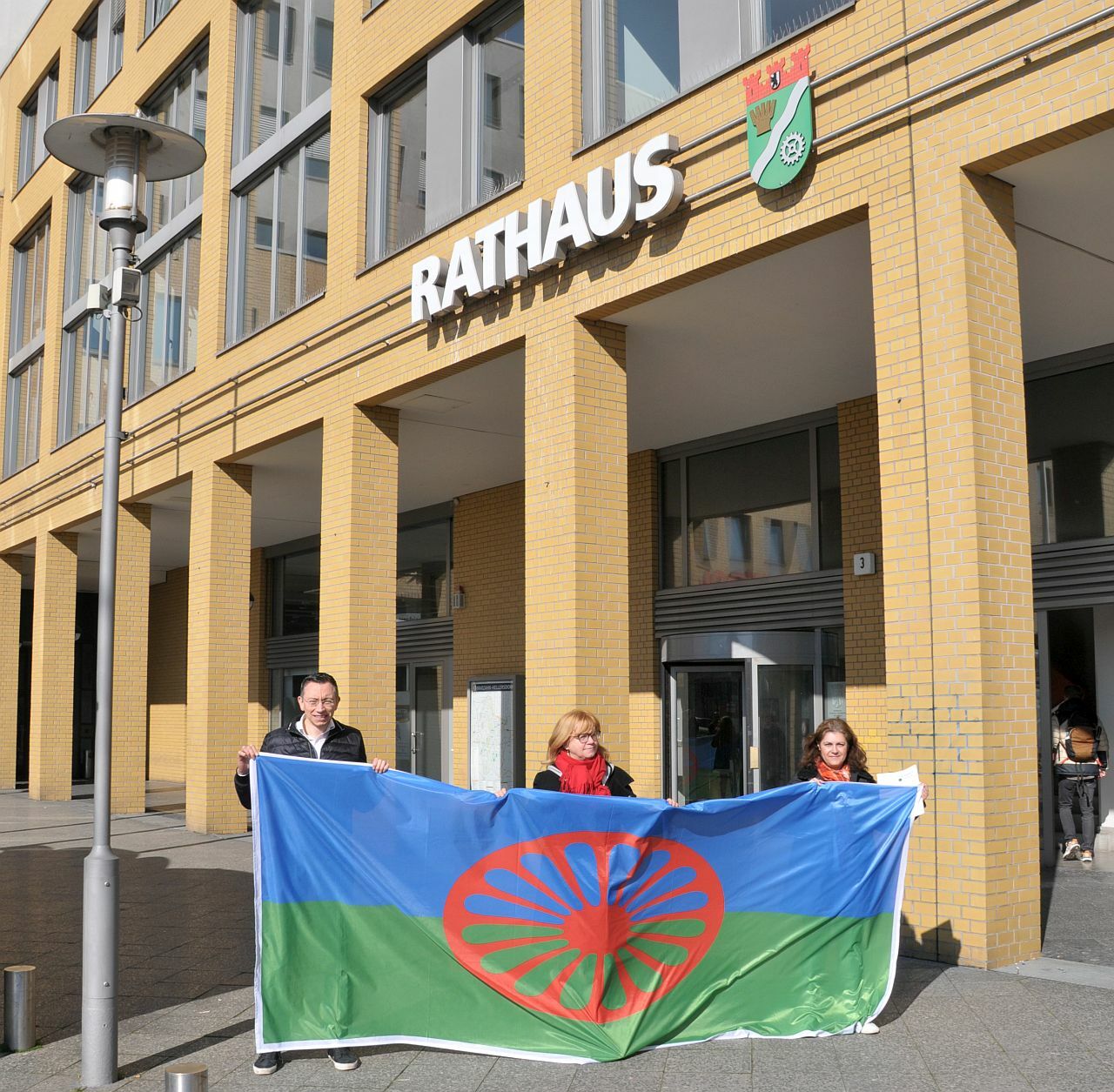Die Fahne der Roma vor dem Rathaus Marzahn-Hellersdorf, gehalten von Juliane Witt, Mariela Nikolova und Prof. Dr. Thomas Bryant