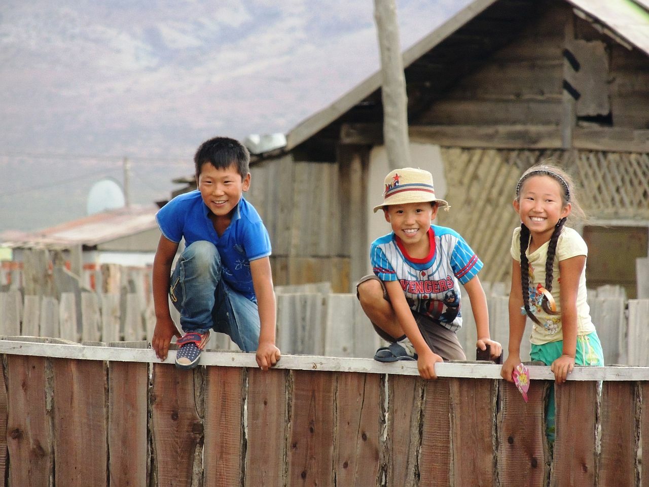 Drei Kinder sitzen auf einem Zaun und lachen in die Kamera