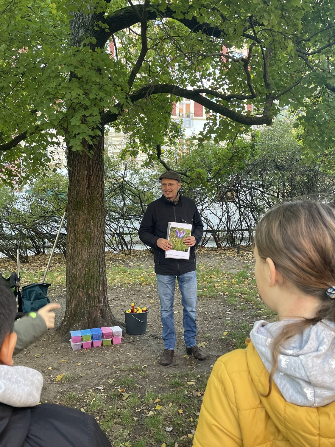 Ein Mann steht mit einem Buch, auf dem ein Krokus abgebildet ist, auf einer Grünfläche.