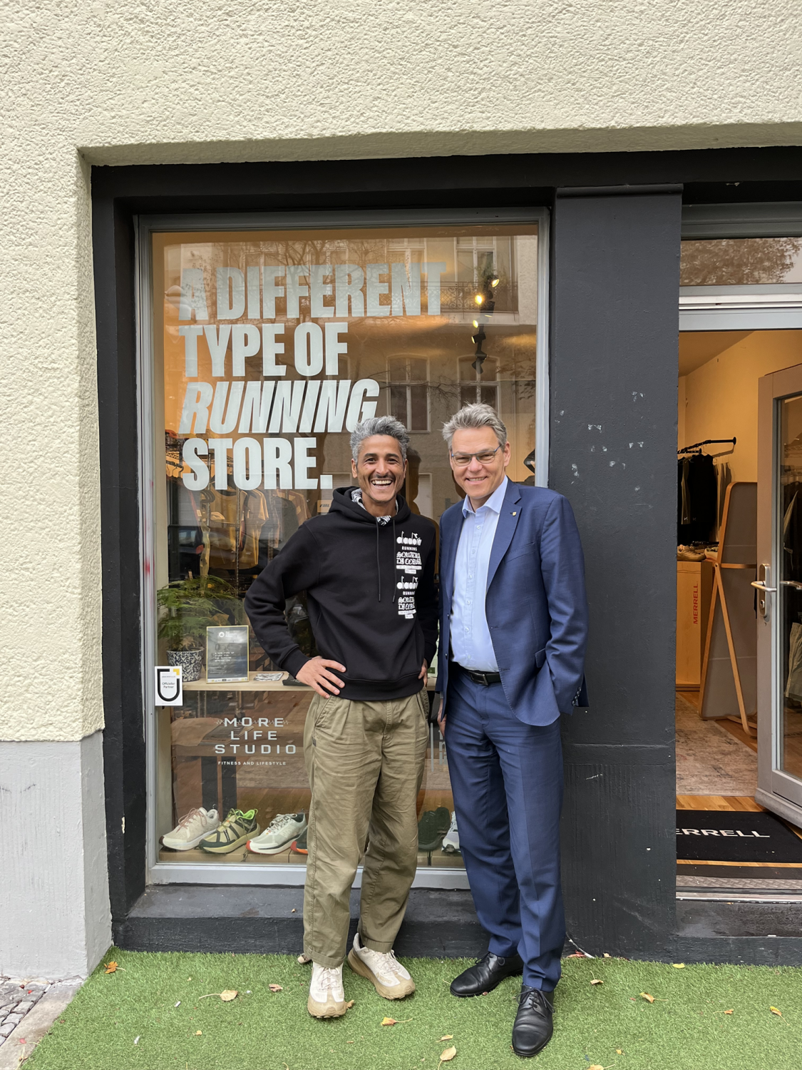 Zwei Männer stehen vor einem Laden. Auf der Fensterfront des Ladens steht der Schriftzug: A different type of running store.