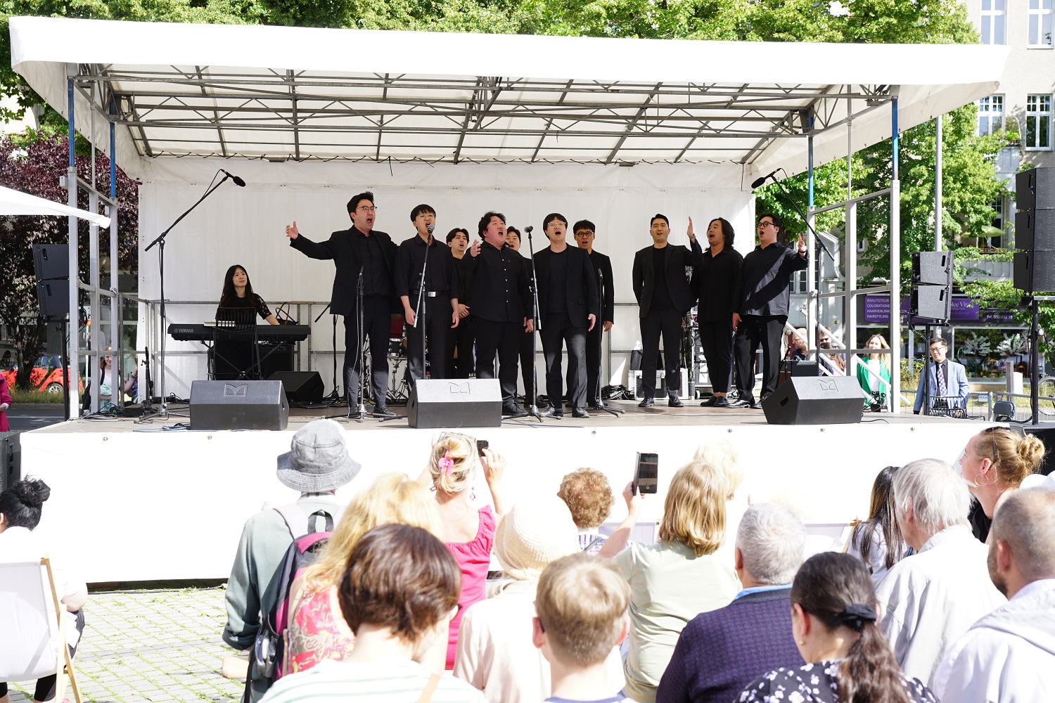 viele Menschen stehen vor einer Open-Air-Bühne, auf der mehrere in schwarz gekleidete Männer stehen