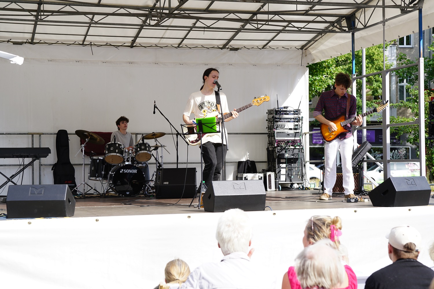 drei junge Menschen, die auf einer Open-Air-Bühne musizieren