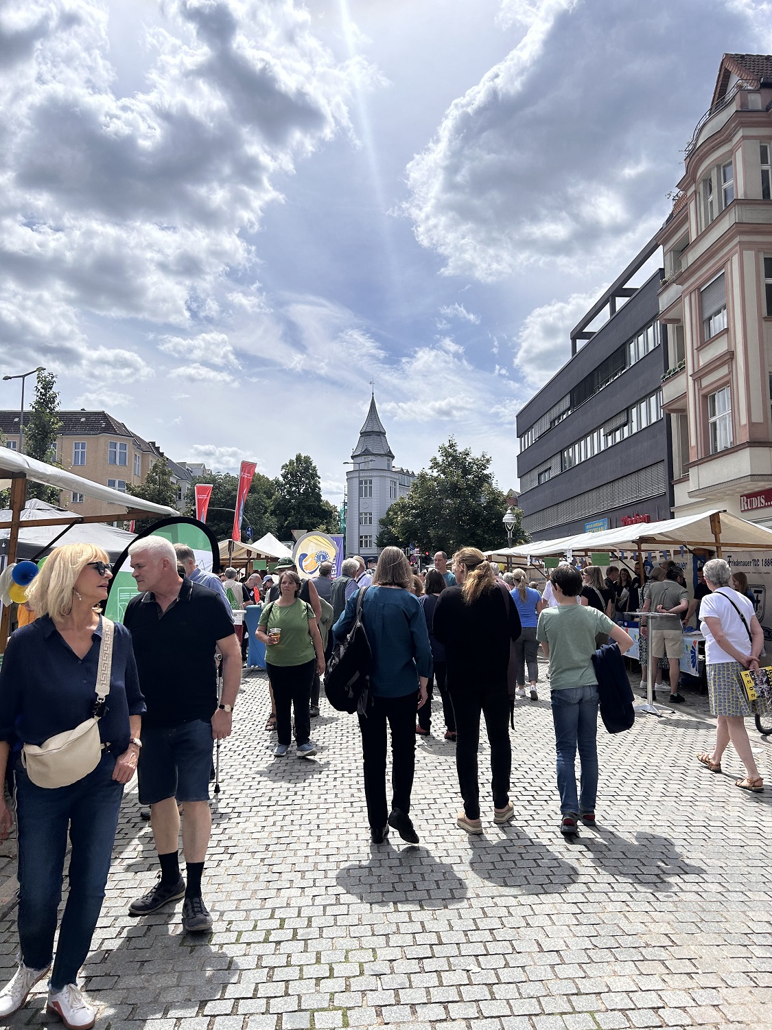 Blick in eine Gasse aus Marktständen, in der Passant_innen unterwegs sind