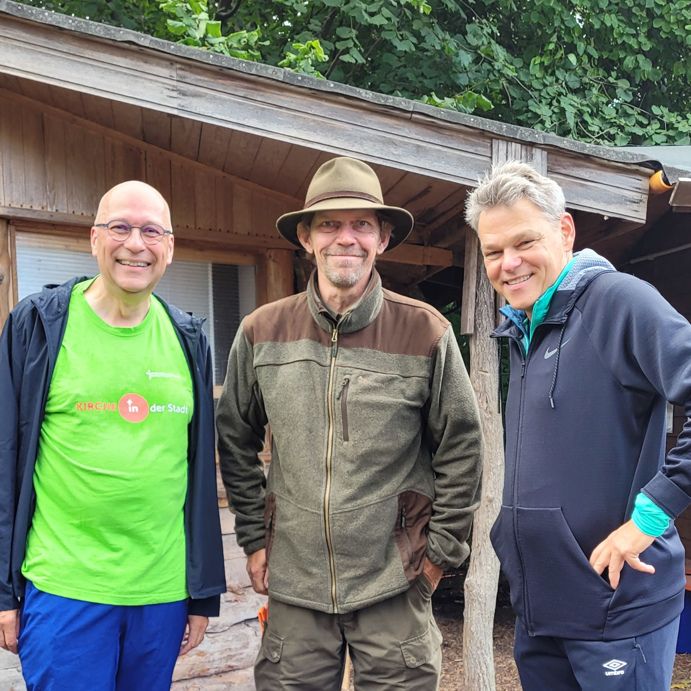 Drei Herren vor einem Holzhaus