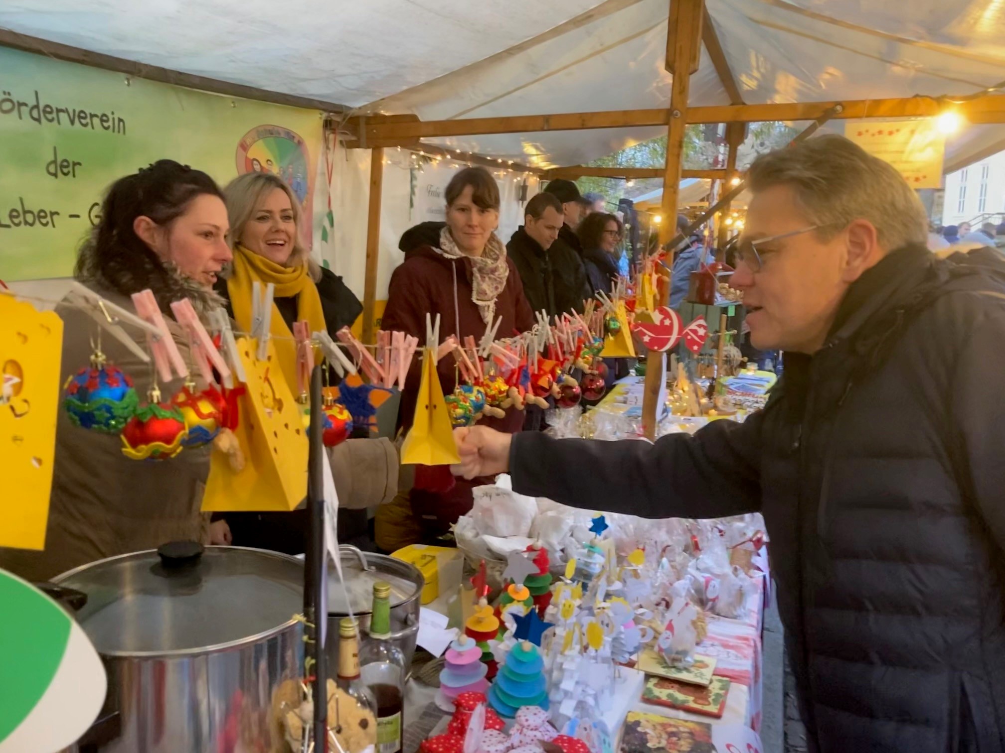 Mann begrüßt Frauen an einem Stand mit Weihnachtsdeko