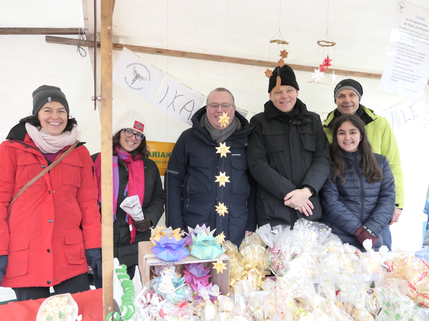 6 Menschen an einem Stand lächeln in die Kamera