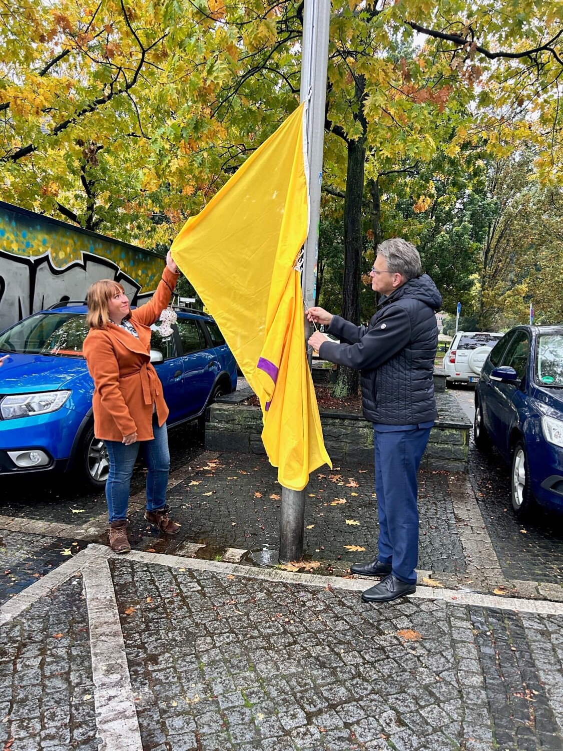 Eine Frau und ein Mann hissen eine gelbe Fahne mit lila Kreis.
