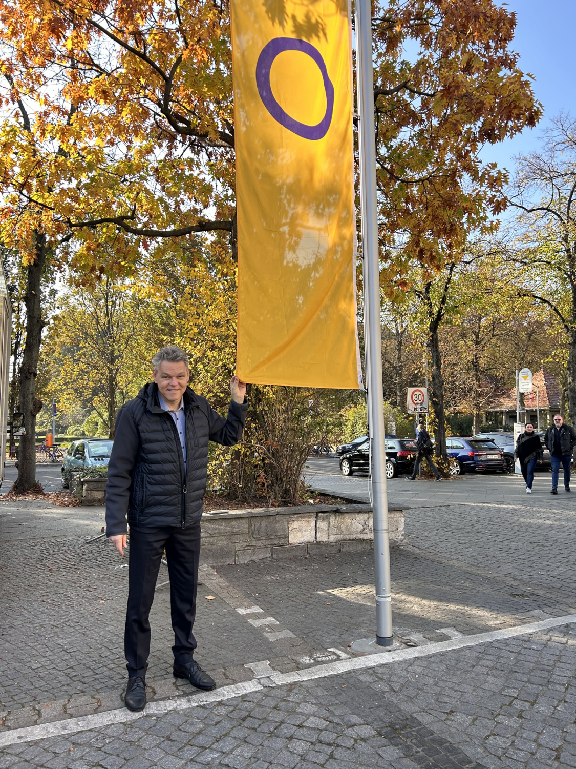 Ein Mann steht neben einem Fahnenmast und hält das Ende einer gelben Flagge mit einem lila Kreis.