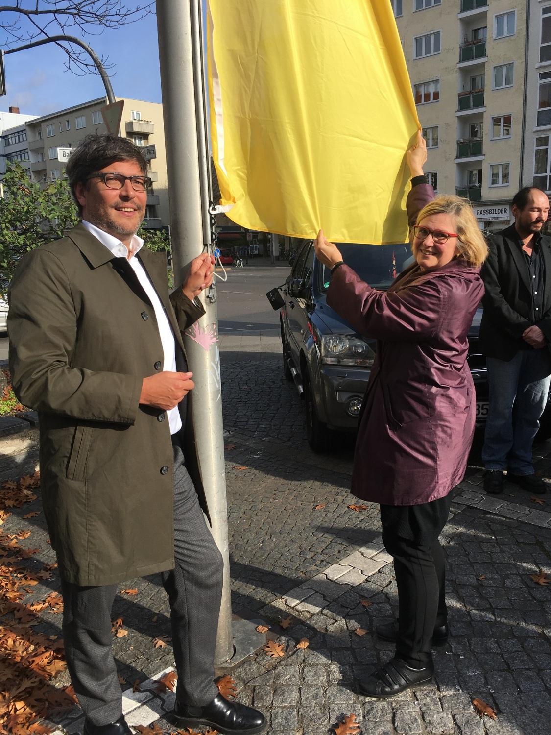 Eine Frau und ein Mann hissen eine gelbe Fahne mit lila Kreis.