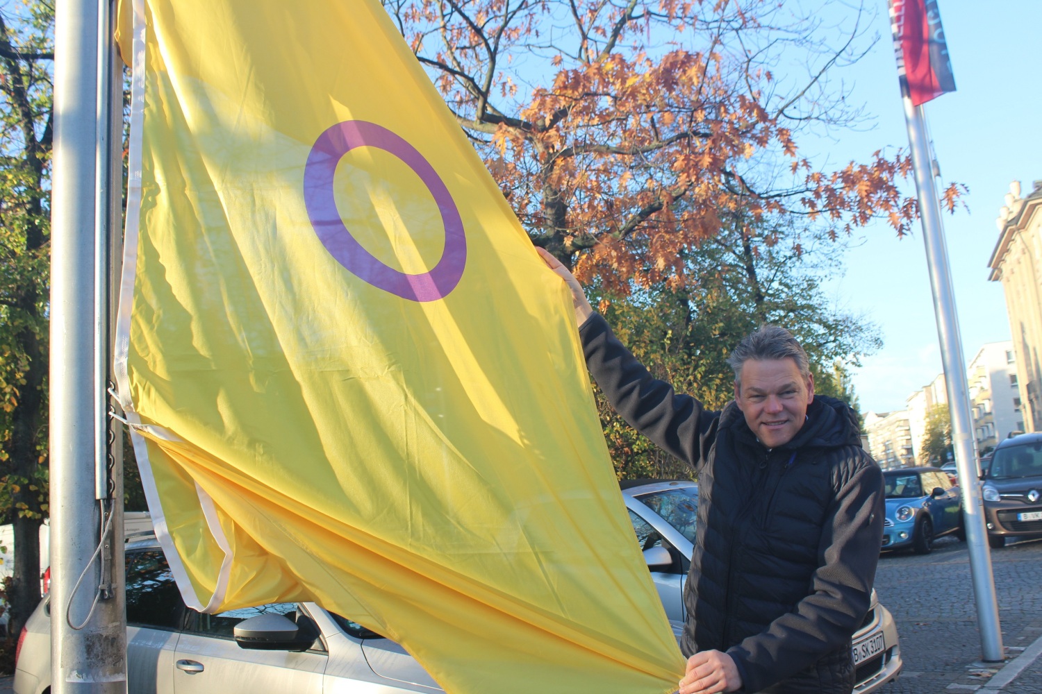 Ein Mann hält eine gelbe Flagge mit lila Kreis an einem Fahnenmast hoch.