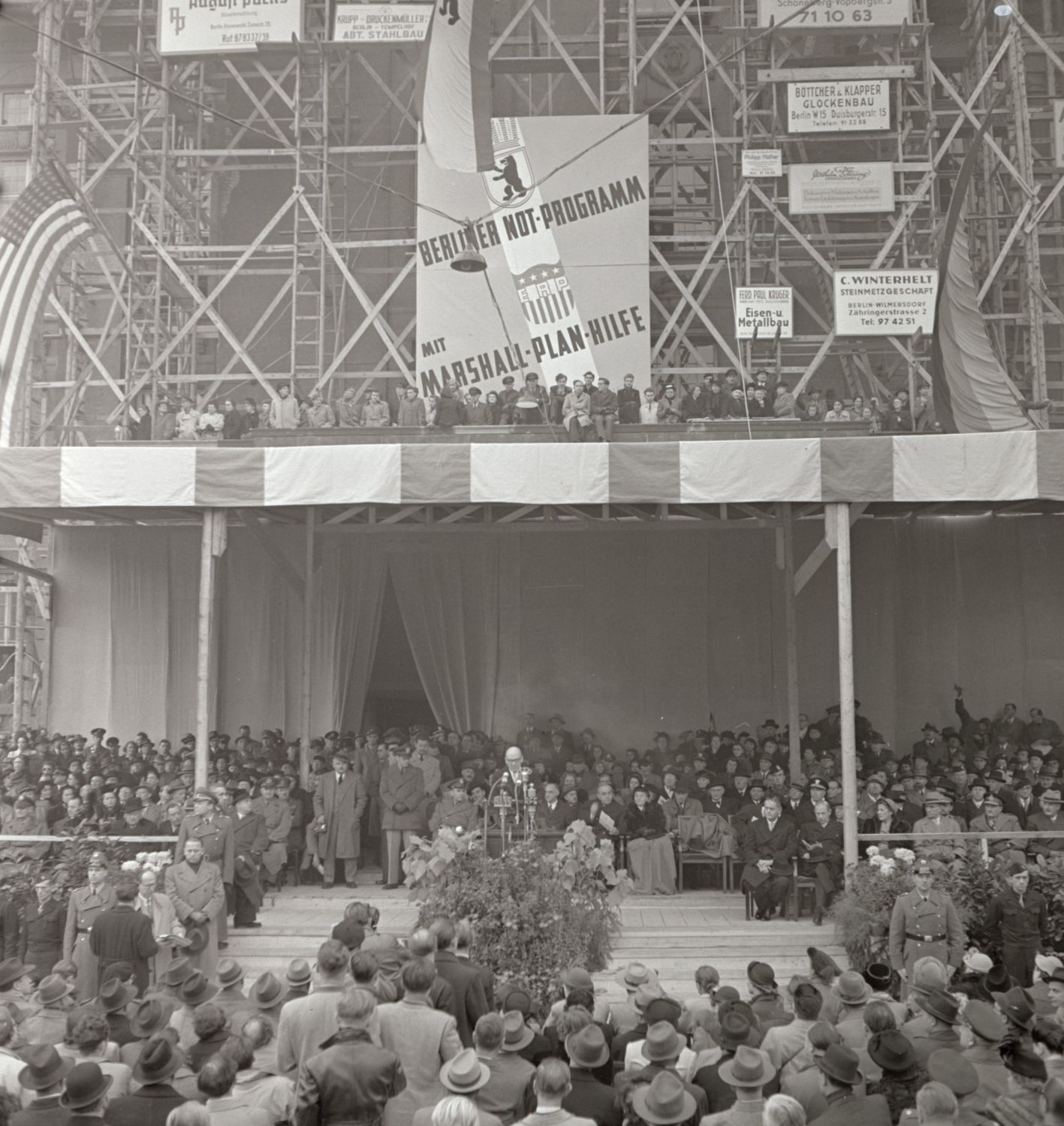 A man is standing behind a lectern, surrounded by a big audience.