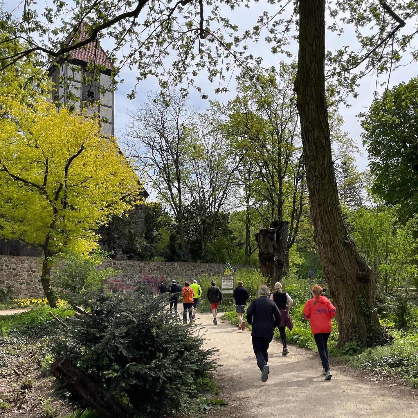 mehrere Personen joggen durch einen Park in Richtung eines hohen Turms