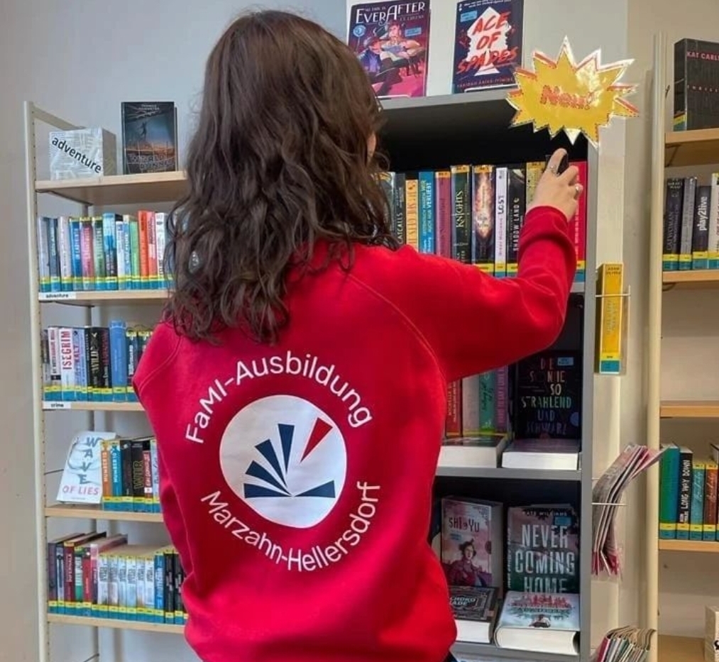 Auszubildende mit rotem Sweatshirt und dem Bibliothekslogo darauf