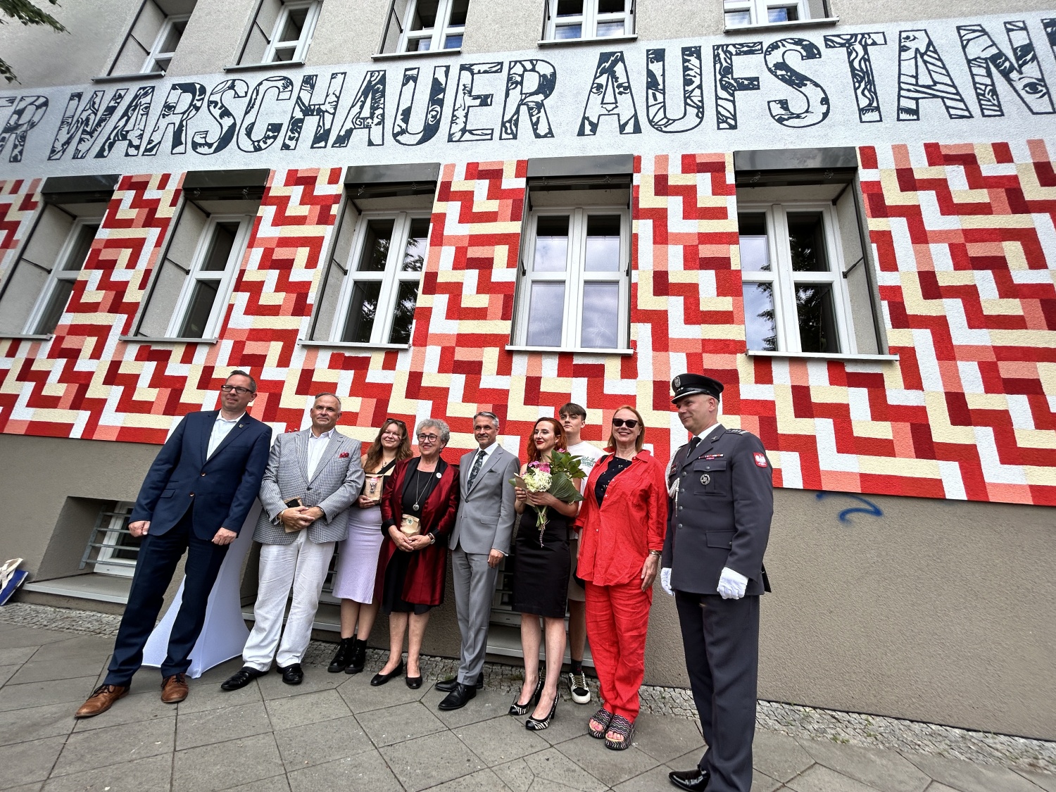 Interessierte Personen und Akteure vor dem Wandbild zum Gedenken an den Warschauer Aufstand