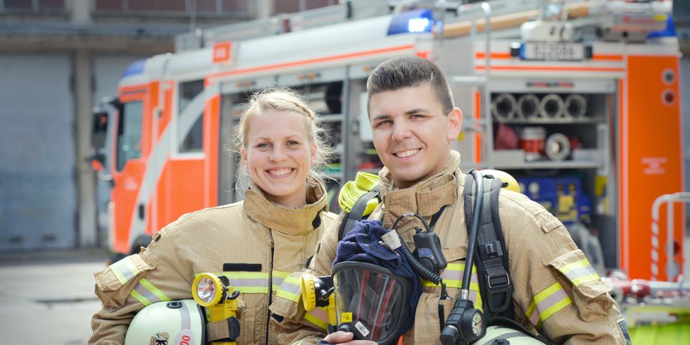 Feuerwehrfrau und Feuerwehrmann vor einem Einsatzfahrzeug