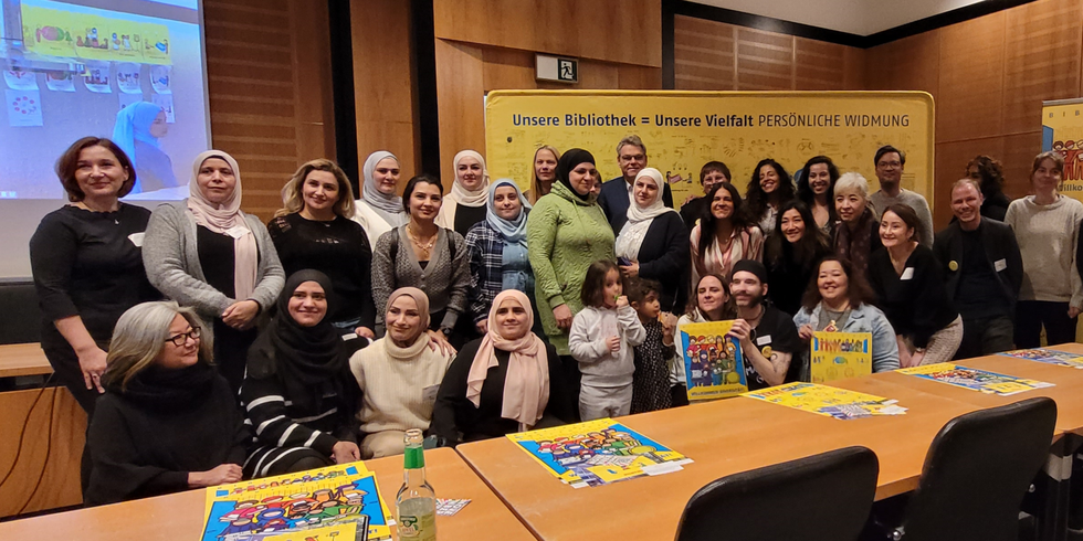 Ein Gruppenfoto vor einer Wand mit der Überschrift: Unsere Bibliothek = Unsere Vielfalt, Persönliche Widmung.