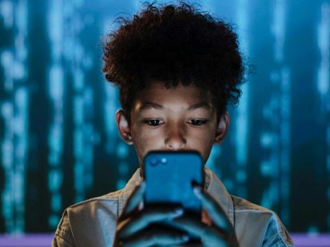 Kind schaut auf sein Handy vor einem blauen Matrix-Hintergrund