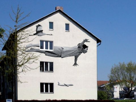 Bildvergrößerung: Auf der Fassade von einem Haus ist ein schwarz-weiß Bild von einem scheinbar fliegendem Kind.