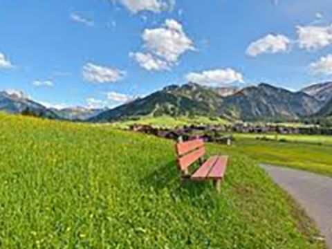 Blick aus dem Tannheimer Tal in Österreich auf die Alpen, im Vordergrund eine Bank auf einer Wiese an einem Weg