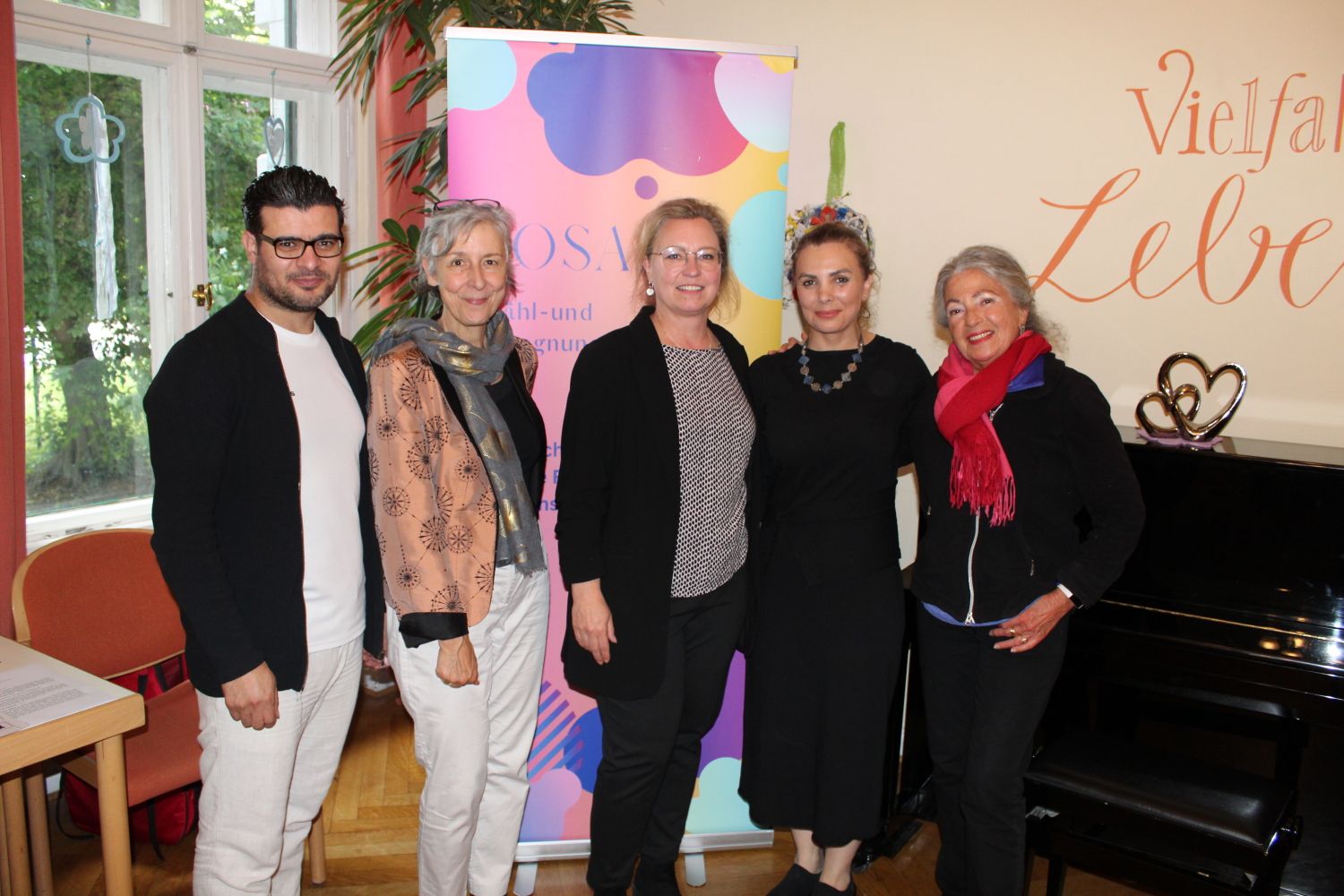 11. Juni 2024: Gruppenbild vor dem Mosaik-Logo mit der Freizeitstättenleiterin Stefanie Müller (Bildmitte) und den Mitgliedern der Mosaik Erzähl- und Begegnungswerkstatt (v.l.n.r.) Hareth Almukdad (Stadtteilarbeiter), Dr. Rita Zobel (Projektleiterin), Boshra Mustafa (Künstlerin), Yvonne Schmitt (Islamwissenschaftlerin).