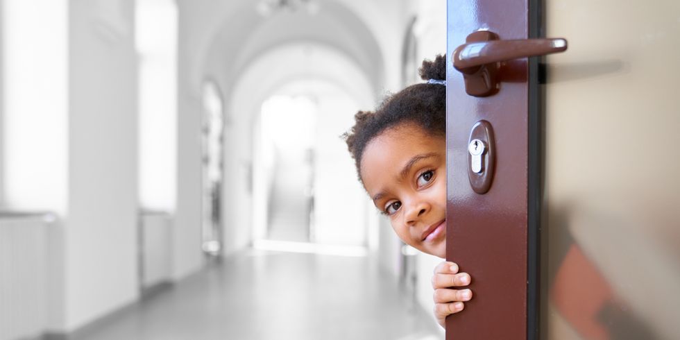 Pretty African girl hiding from opened door in school.