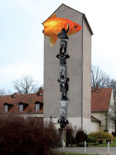 Auf einem Turm ist ein großes Bild zu sehen. Das Bild zeigt mehrere Jungs in schwarz-weiß. Der oberste junge streckt sich zu einem großen orangenen Goldfisch.